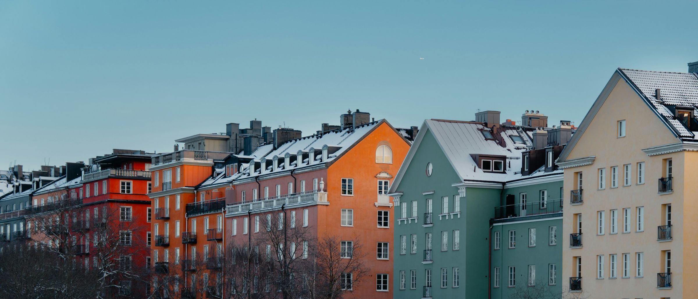Värikkäitä kerrostaloja lumisine kattoineen kirkasta taivasta vasten