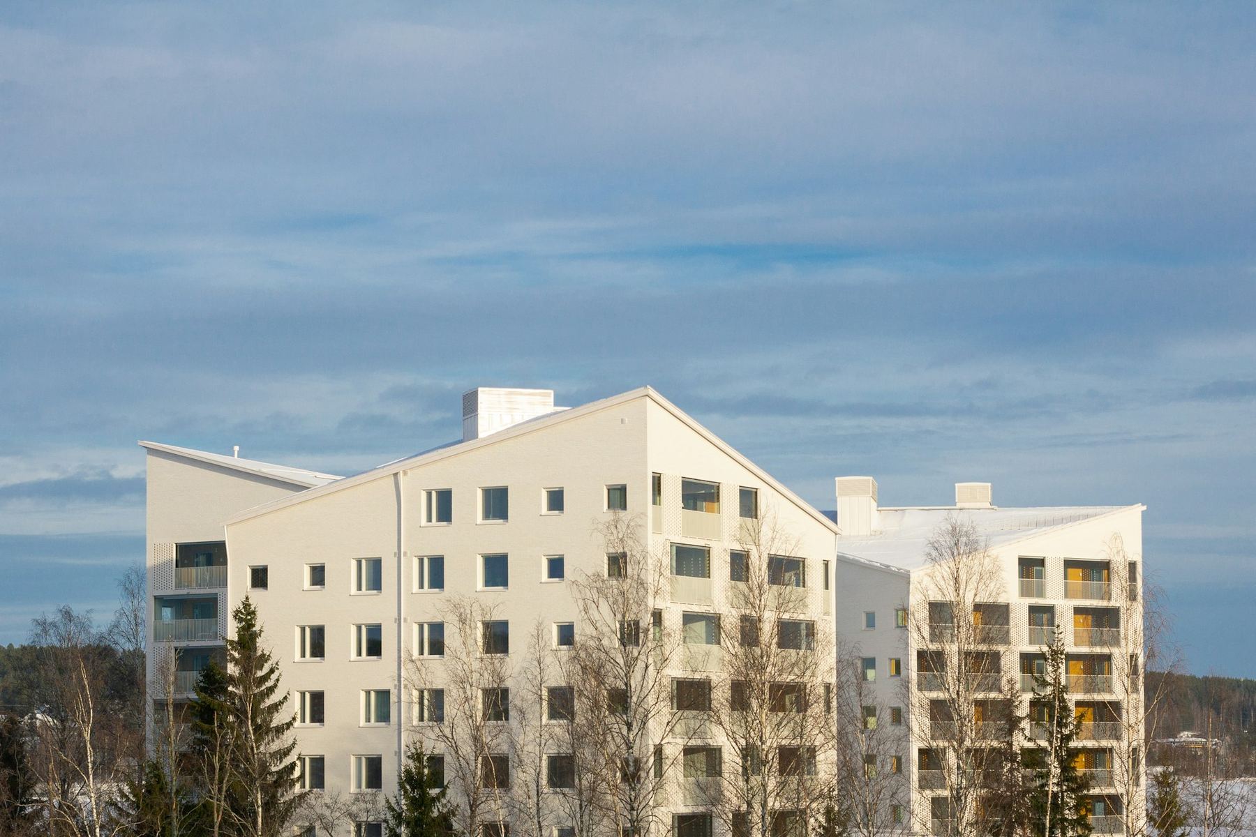 Vaalea kerrostalo metsän reunalla